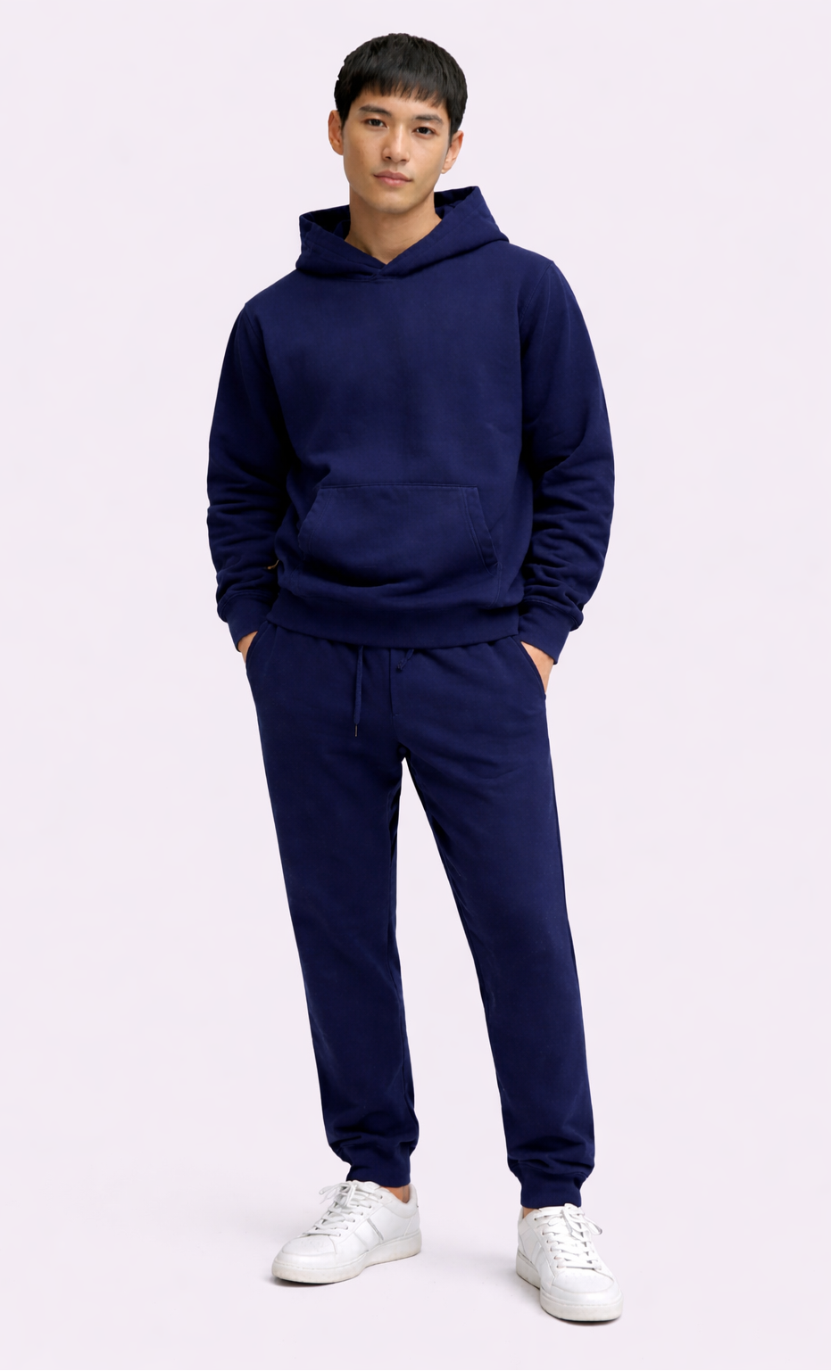 Person wearing a navy blue hoodie and jogger set with white sneakers on a light purple background