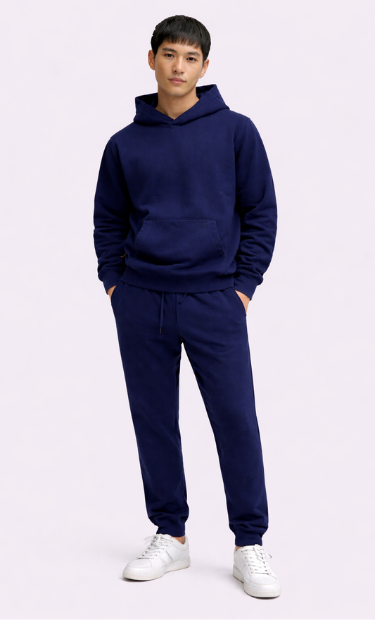 Person wearing a navy blue hoodie and jogger set with white sneakers on a light purple background